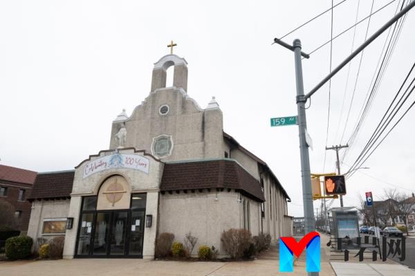 The exterior of our lady of grace church near a street sign of 159 avenue, with a banner over the door reading celebrating 100 years