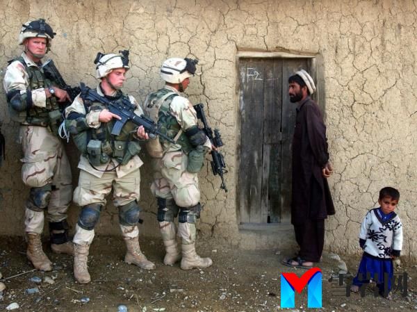 A picture of an Afghan man and his son looking at American soldiers who are outside of their home.